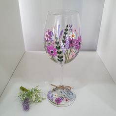 a wine glass with flowers painted on it next to a flower sticker and lavender sprig