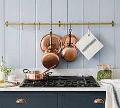 pots and pans are hanging on the wall above an oven in a kitchen with blue cabinets