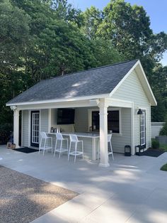 a small house with white chairs and a bar in the back yard on a sunny day