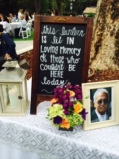 a table with flowers and pictures on it, next to a sign that says this lantern is lit in loving memory so those who could be here today