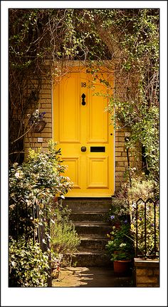 a yellow door is in the middle of some bushes and trees, with stairs leading up to it