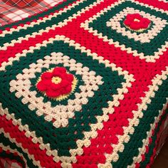 a crocheted blanket on top of a bed covered in red, green and white squares