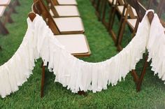 a row of wooden chairs with white ruffles hanging from the back of them