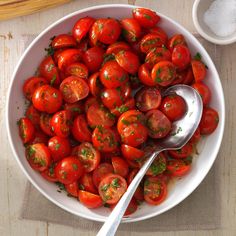 a white bowl filled with lots of cherry tomatoes next to a spoon and some seasoning