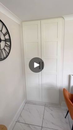 a room with white walls and a clock on the wall next to a chair in front of it