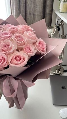 a bouquet of pink roses sitting on top of a white table next to a laptop