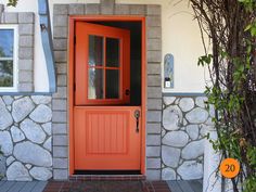 an orange front door on a house with stone wall and brick walkway leading up to it