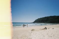 people are walking on the beach with surfboards