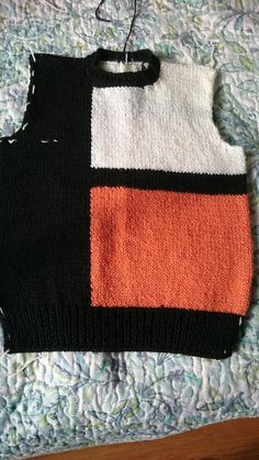 a black, white and orange sweater hanging from a hook on top of a bed