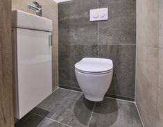 a white toilet sitting inside of a bathroom next to a wall mounted dryer and sink