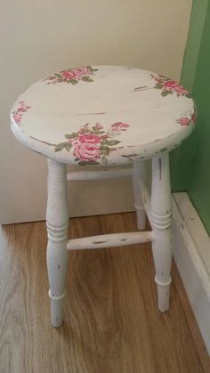 a white stool with pink roses painted on the top and bottom, sitting in front of a green wall