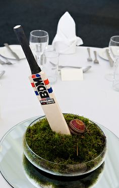 a cricket bat sitting on top of a moss covered bowl at a table with wine glasses and silverware