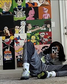 a person sitting on the floor with their cell phone in front of a wall full of cartoon pictures