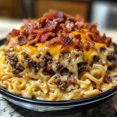 a black bowl filled with noodles covered in cheese and bacon sitting on top of a table