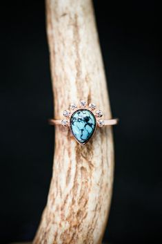 a turquoise stone ring sitting on top of a piece of driftwood in front of a black background