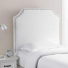 a white bed sitting next to a night stand with a clock on top of it