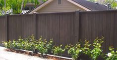 a brown fence with flowers growing on the side of it and a house in the background