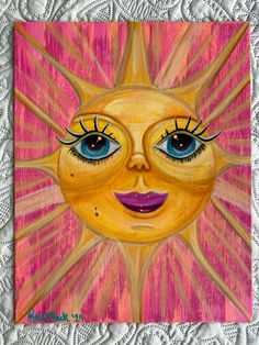 a painting of a sun with blue eyes on a white lace doily, in pastel and acrylic colors