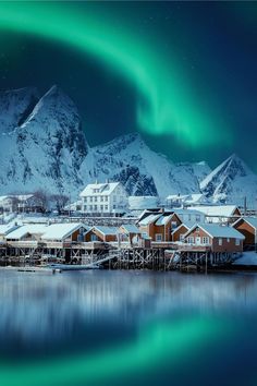 the northern lights shine brightly over houses and snow - capped mountains in this winter scene