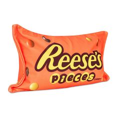 an orange pillow with reese's pieces printed on the front and sides, sitting on a white surface