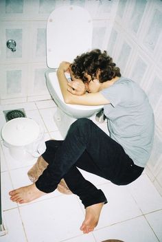 a woman sitting on the floor in front of a toilet with her head resting on the seat