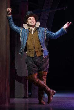 a man in a blue jacket and hat on stage with his arms out to the side