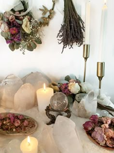 a table topped with lots of different types of flowers and candles next to crystal rocks