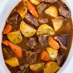 a white bowl filled with beef stew and carrots on top of a wooden table