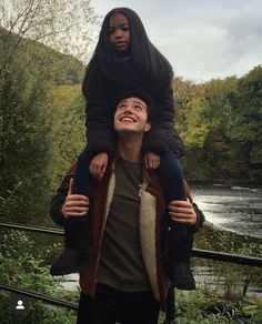 a man carrying a woman on his shoulders in front of a river with trees and bushes