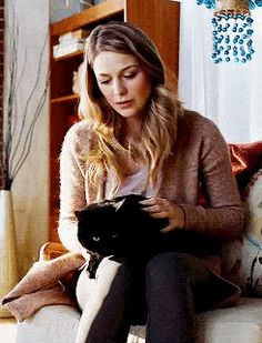 a woman sitting on a couch holding a black cat