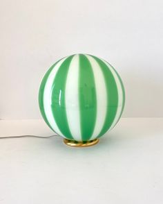 a green and white striped glass ball lamp on a gold plated base with a cord plugged in