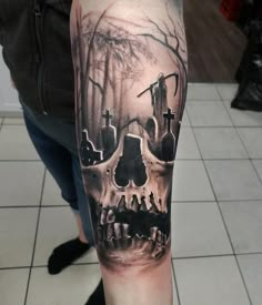 a man's arm with a skull and graveyard scene tattoo on the left upper arm