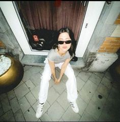 a woman sitting on the ground in front of a door with sunglasses on her face