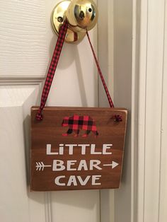 a little bear cave sign hanging on a door handle with a red and black checkered ribbon