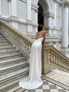 a woman in a white dress is standing at the top of some stairs with her back to the camera