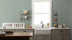 a kitchen with yellow brick walls and gray cabinets, white sink and window in the corner