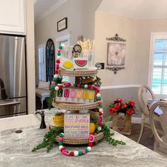 a three tiered cake is decorated with letters and decorations on the table in front of a kitchen