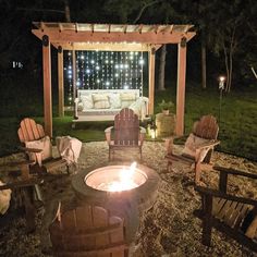 an outdoor fire pit with chairs around it and lights shining on the wall behind it