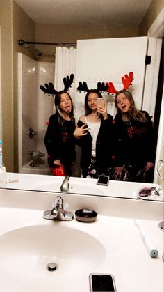 three women are taking a selfie in the bathroom with reindeer antlers on their head