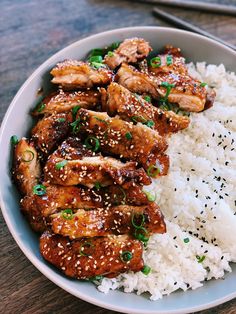 a white bowl filled with rice and chicken on top of a wooden table next to chopsticks