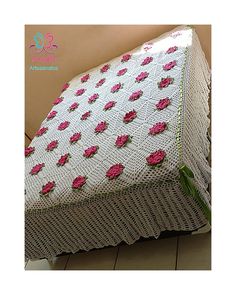 a white crocheted blanket with pink flowers on it