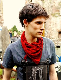 a young man wearing a red scarf around his neck is standing in front of an old building