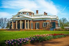 a large brick building with many flowers in the foreground and a walkway leading up to it