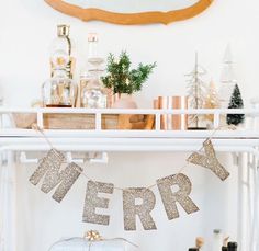 a merry banner is hanging on a white shelf in front of a mirror and other holiday decorations