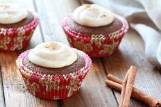 three cupcakes with frosting and cinnamon on a wooden table next to cinnamon sticks