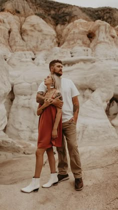 a man and woman standing next to each other in front of some white rocks with their arms around each other