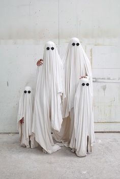 three white ghost statues standing next to each other in front of a wall with eyes on them