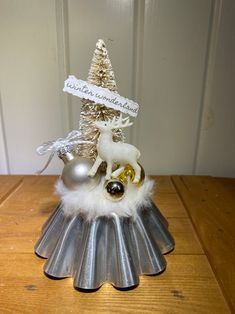 a small christmas tree on top of a tin pan with ornaments in it and a ribbon around the base