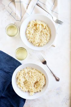 two white bowls filled with rice next to silverware