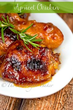 two pieces of chicken on a white plate with sauce and rosemary sprig in the middle